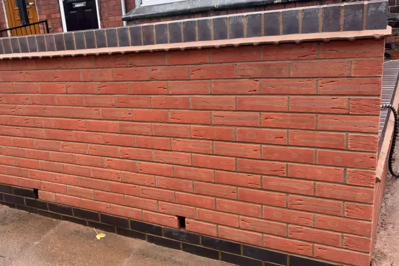 Newly built red brick front garden wall with a blue brick plinth and a blue brick on edge coping