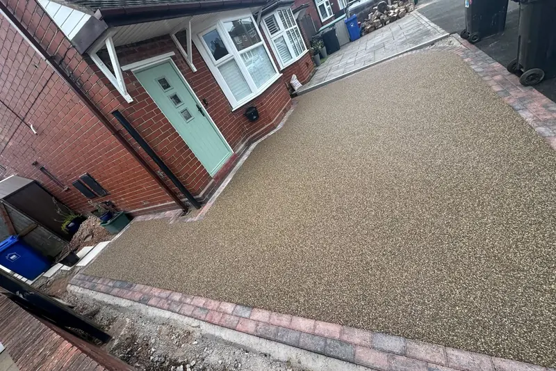 Buff resin driveway with a red block paved edge in front of a terraced house with a sage green door