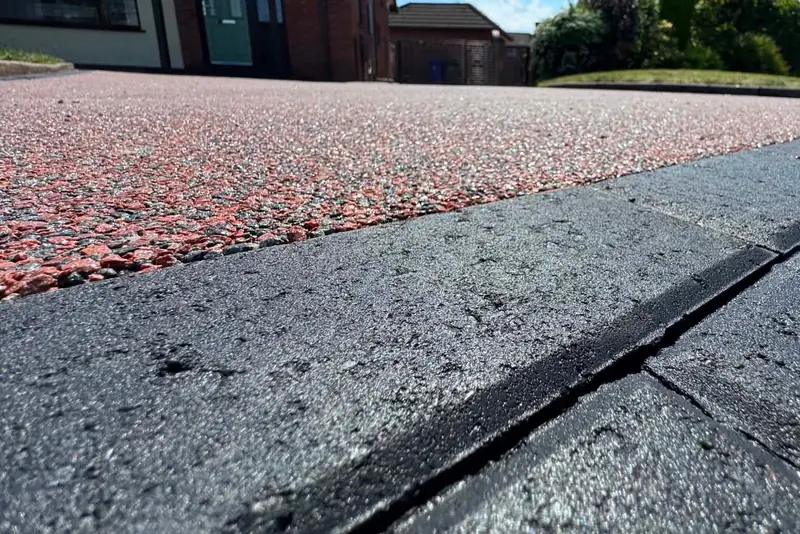 Close-up of a curved charcoal block paved edge beside a red resin driveway