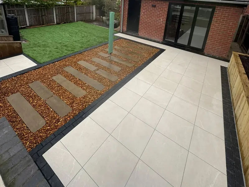 Cream porcelain patio with a charcoal border, stepping stones set in bark and a brick garden room with bifold doors