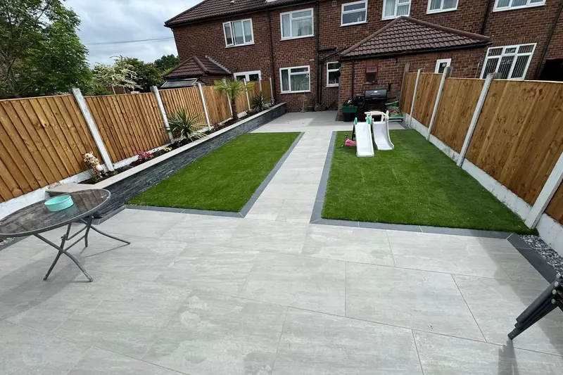 Pale grey porcelain patio with two rectangular artificial lawns edged in charcoal in a fenced back garden