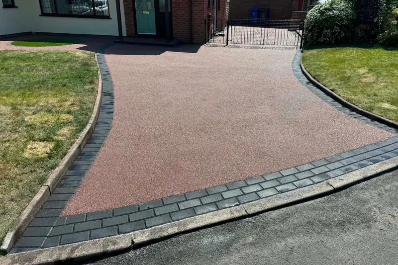 Red resin driveway with a curved charcoal block paved border sweeping from the road up to a bungalow