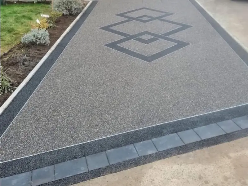 Grey resin driveway with three interlocking diamond shapes inlaid in charcoal resin and a charcoal block border
