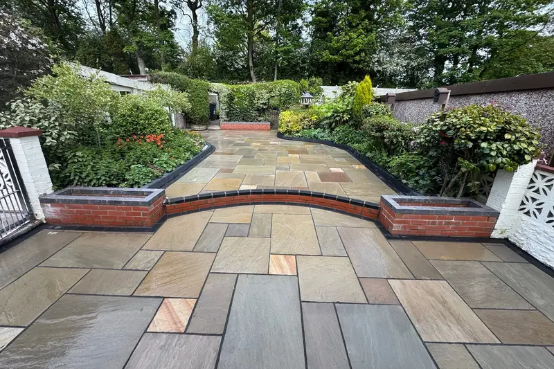 Indian sandstone patio on two levels divided by a curved red brick wall with charcoal coping and planters, surrounded by a mature garden