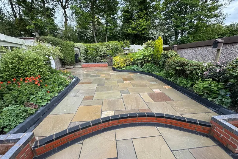 Indian sandstone patio winding through a planted garden with a curved red brick wall in the foreground